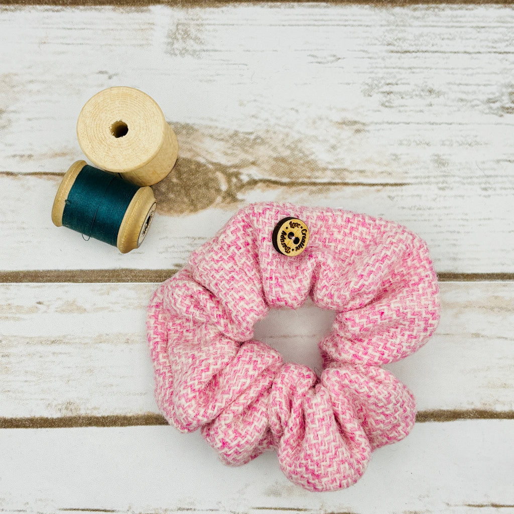 Pink scrunchie with a button on a wooden surface next to a spool of thread.
